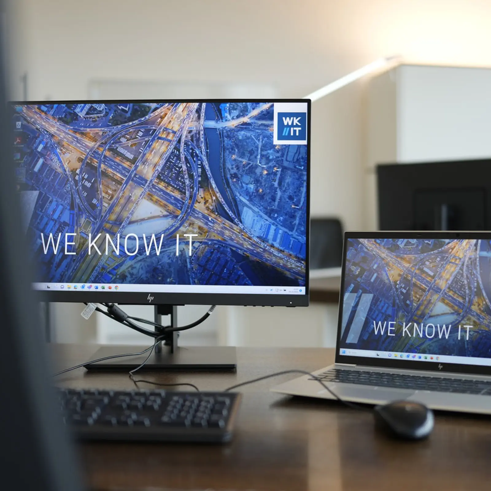 Managed IT Services – Schreibtisch mit HP-Monitor und Laptop, beide mit dem Slogan 'WE KNOW IT' angezeigt.
