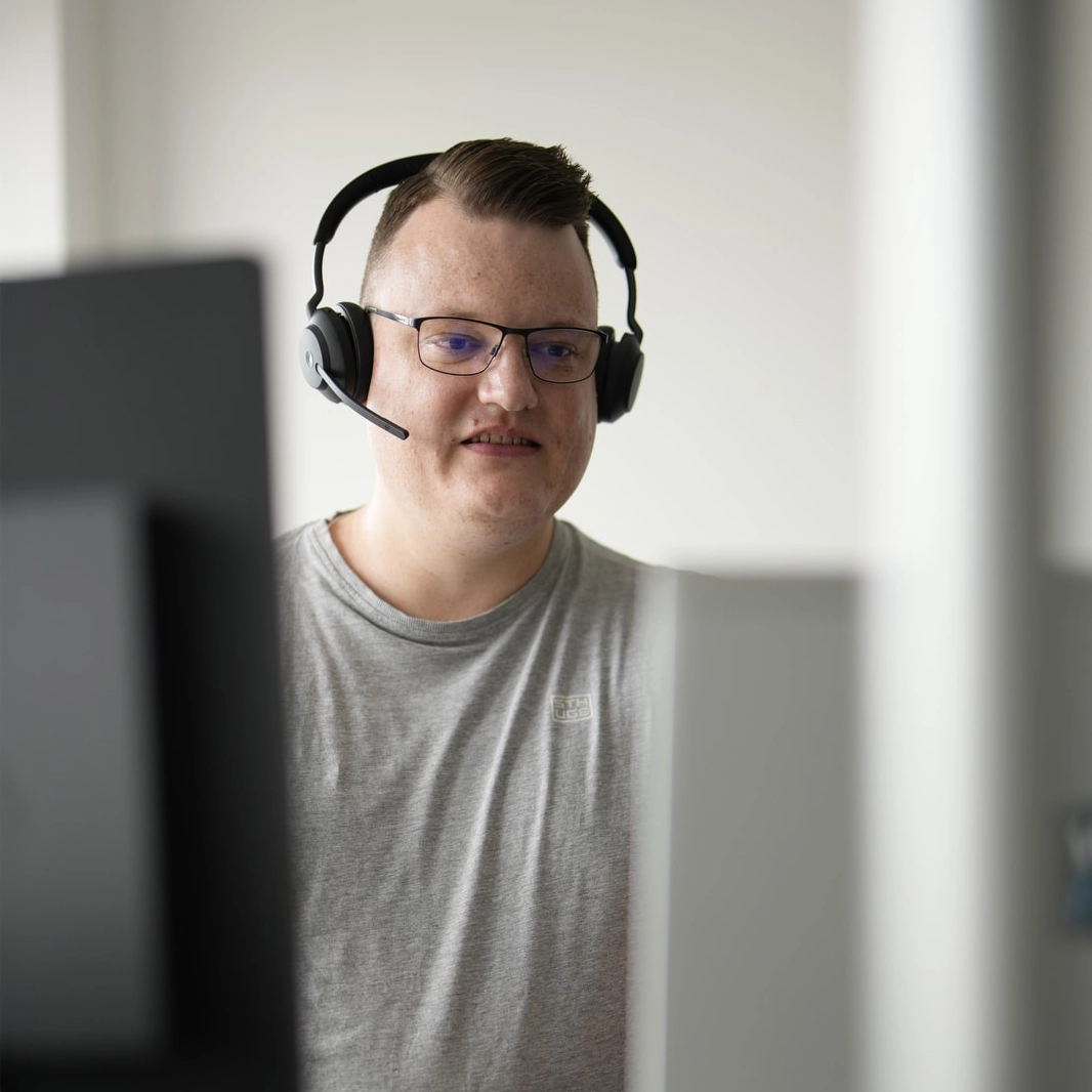 WK IT Berater mit Headset sitzt vor PC-Bildschirm und steht stellvertretend für die Software Services der WK IT.
